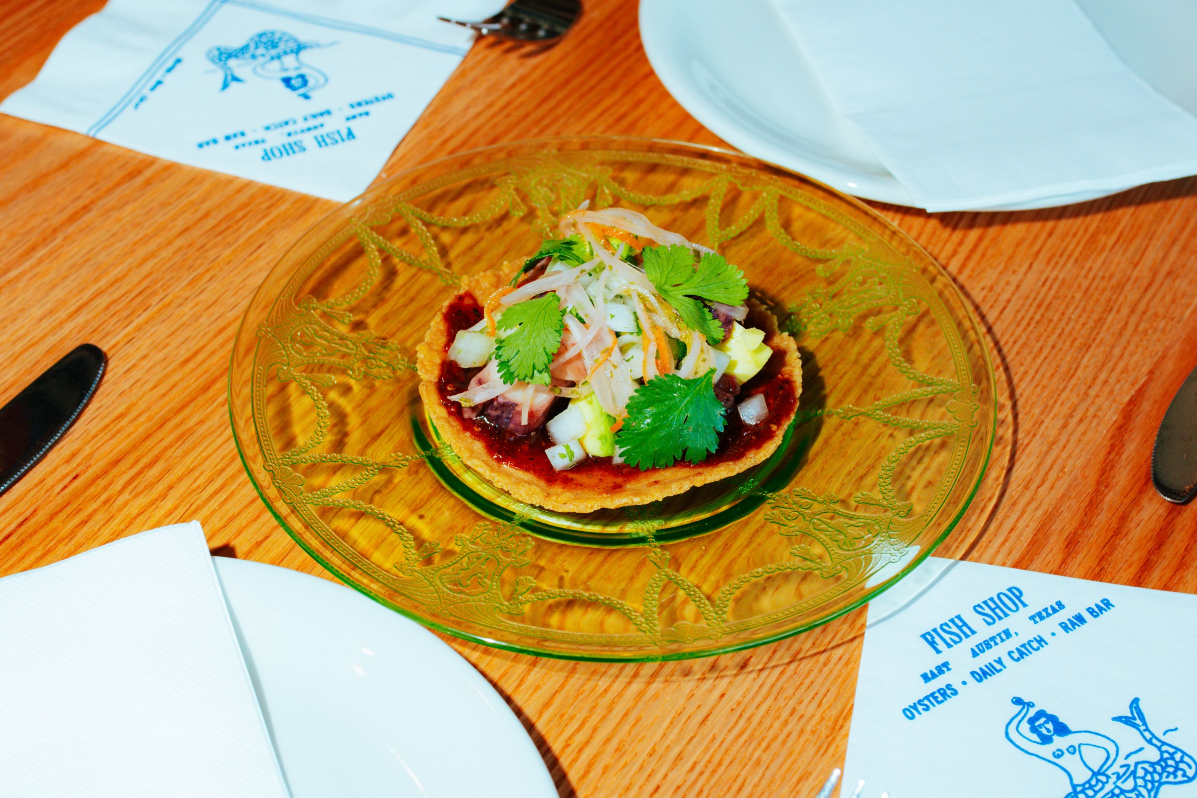 A tostada with octopus topped with cilantro on a clear plate.