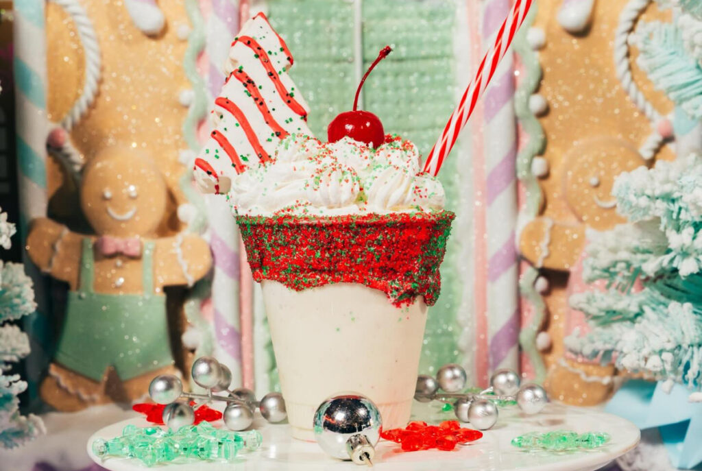 Image shows a seasonal milkshake surrounded by whimsical candy decor for the Land of Sweets holiday pop-up at Serious Eats in Grand Prairie.