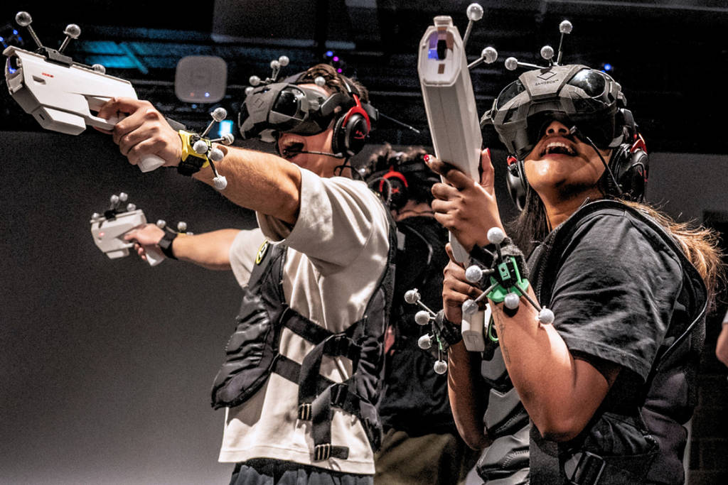 Image shows two players at Sandbox VR equipped in technological gear holding gaming weapons.
