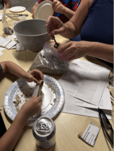Two pairs of hands work with clay on a table.