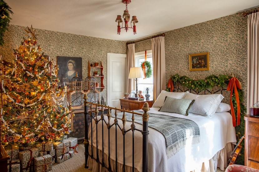 Bedroom with iron bed, garland on headboard, and full-sized Christmas tree in opposite corner.