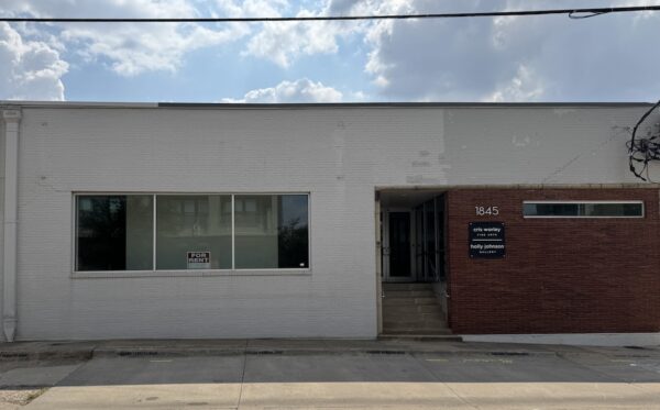 The exterior of a one-story gallery building, with a For Rent sign in the window.