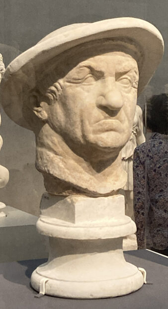 A photograph of a marble sculpture of the head of a man wearing a hat.
