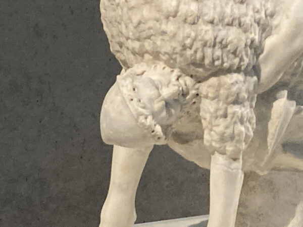 A detail of a statue of a man holding on to the underneath of a ram.