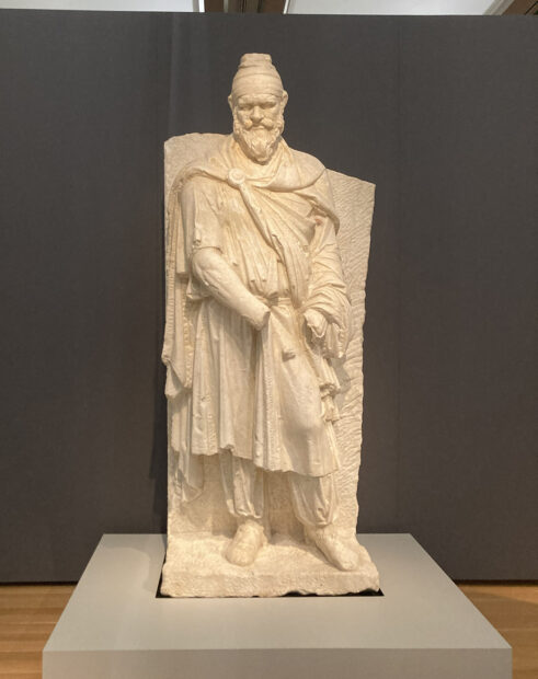 A photograph of a marble sculpture of a fully clothed bearded man.