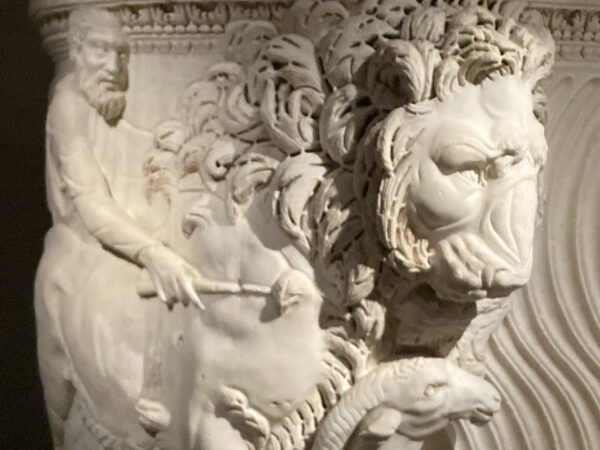 A close-up photograph of a sarcophagus featuring a man and a lion.