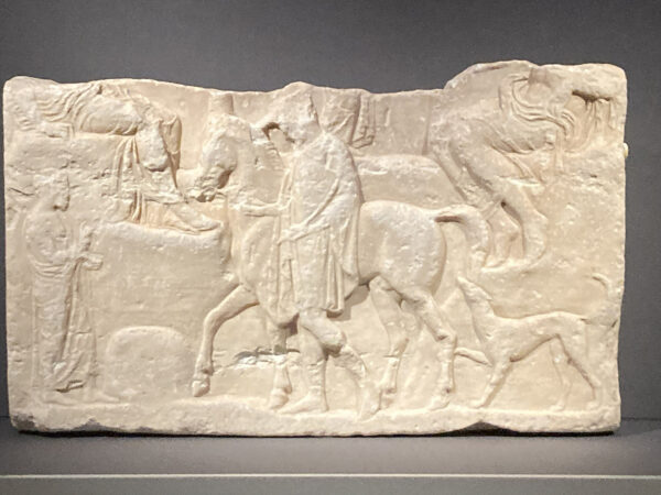 A photograph of a marble relief featuring a figure and a horse. 