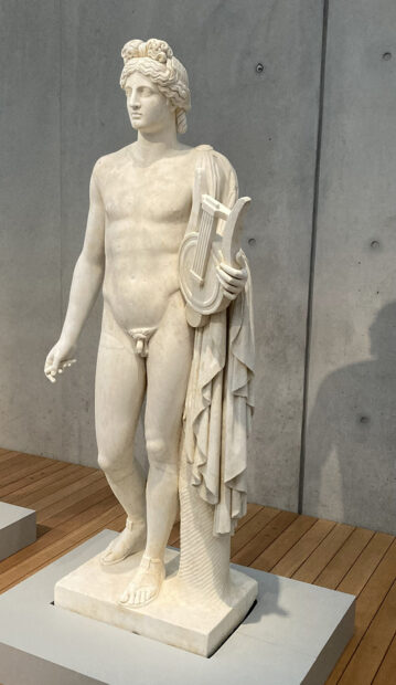 A photograph of a marble sculpture of a nude male figure holding a lyre.