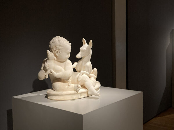 A photograph of a marble sculpture of a young boy with two dogs.