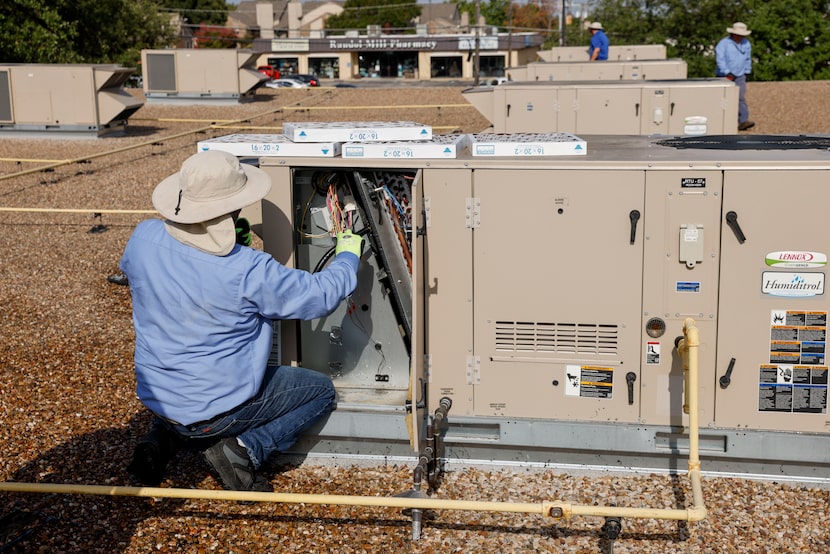 An HVAC mechanic cleans an air conditioning unit on the roof of Wimbish World Language...
