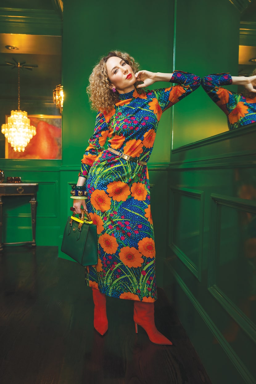 Carla Rockmore in bright orange floral dress and orange suede boots holding green textured...