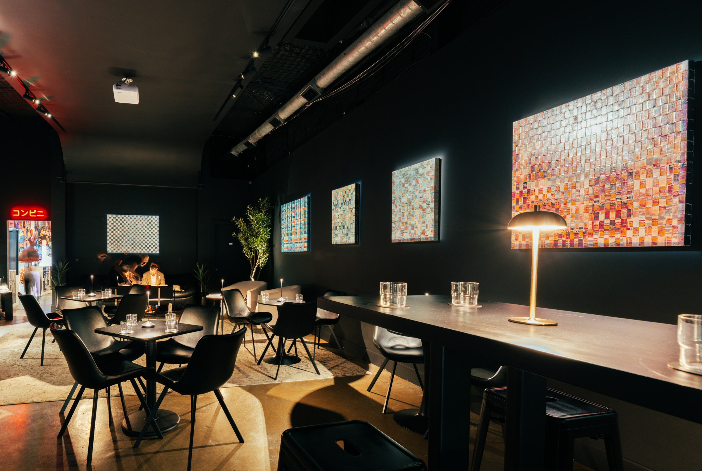 A dark bar with tables and sears with artwork onwalls.