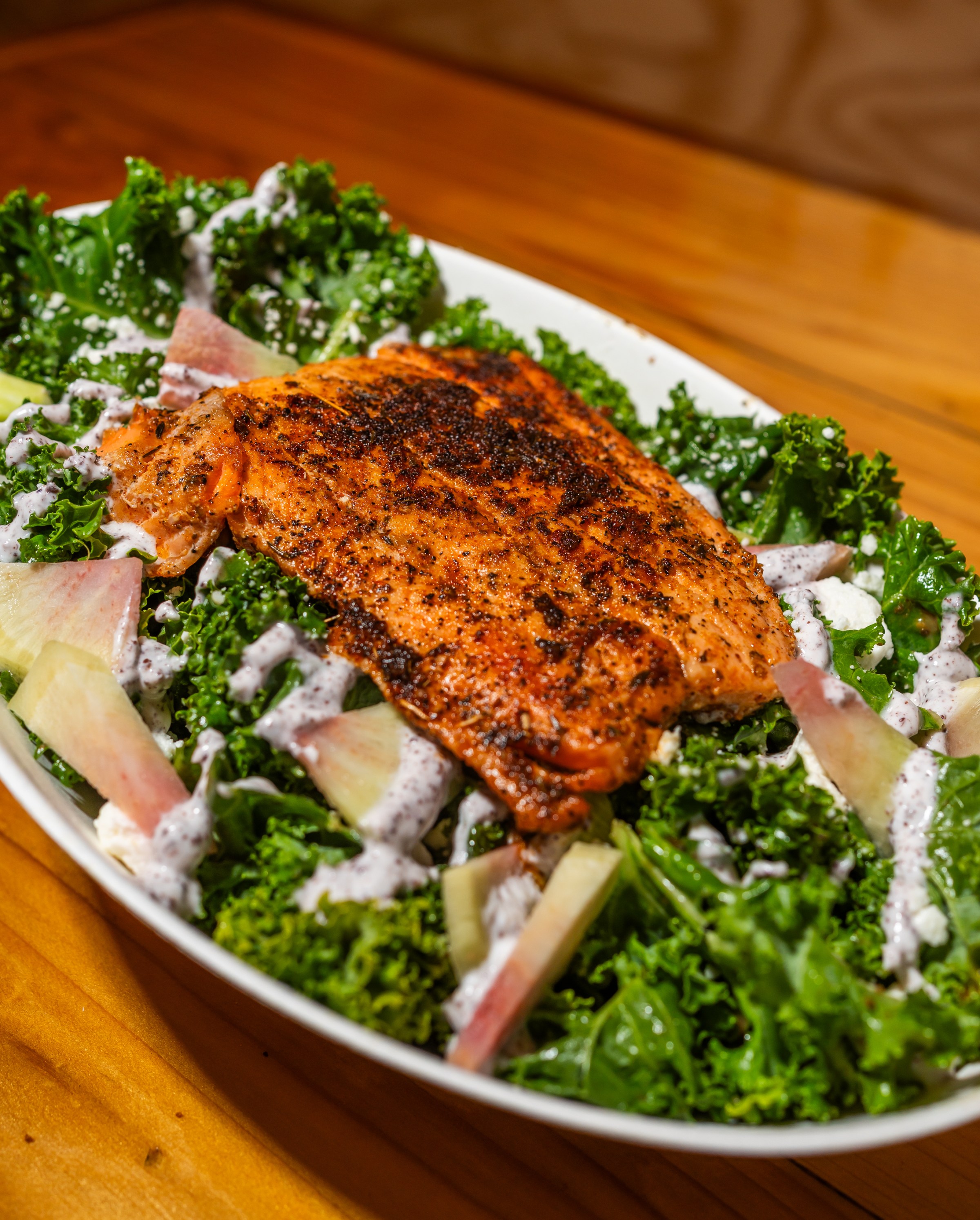 A grilled chicken on a bed of lettuce with white dressing. 