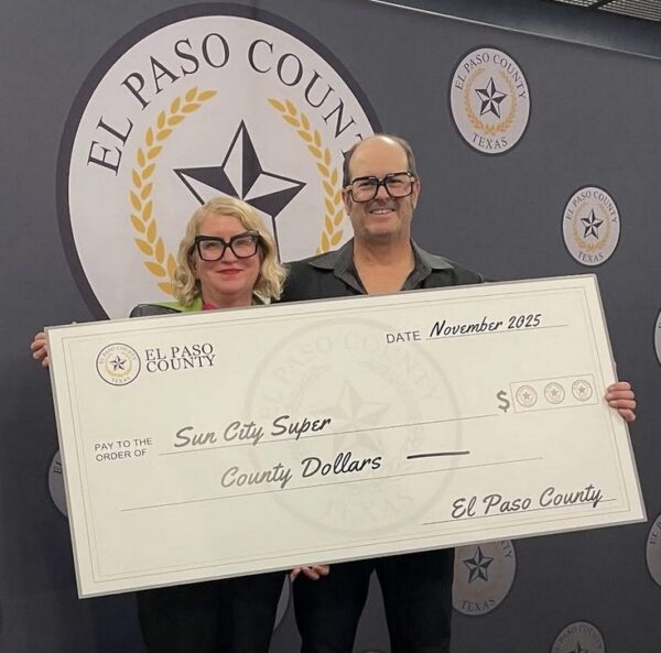 A couple wearing eccentric glasses hold a big check made out to Sun City Super from El Paso County.