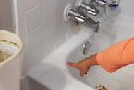 Water runs down the edge of the tub as Guadalupe Arista points out areas of her apartment...