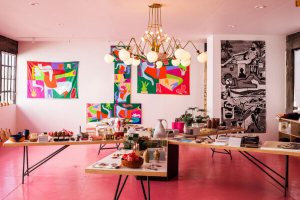 A photograph of the interior of a colorful gallery and store featuring pink floors and wooden tables filled with small art objects and books.