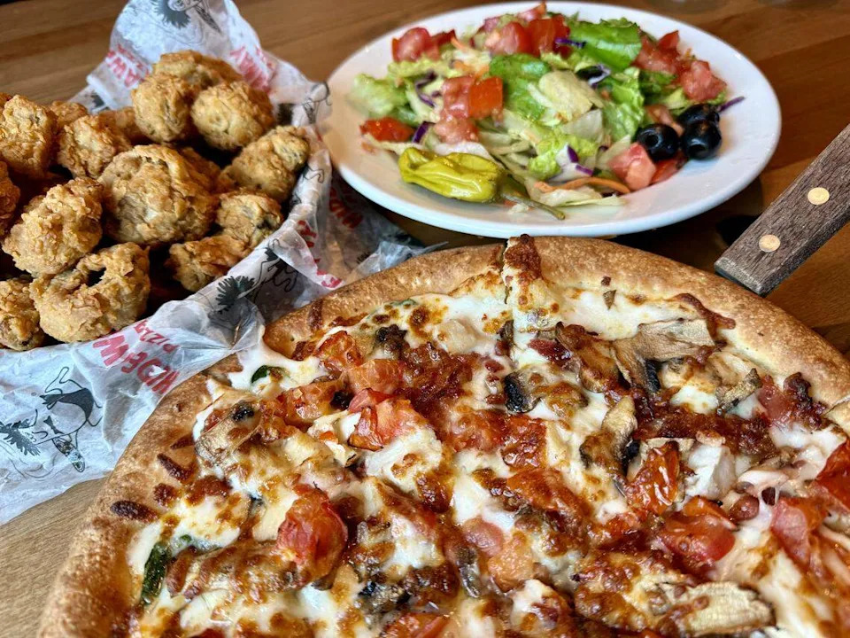 A bacon-chicken-and-spinach Alfredo “Paradise Pie” with thin crust, seen along with fried mushrooms and salad Aug. 23, 2025 at Hideaway Pizza in Fort Worth, Texas.