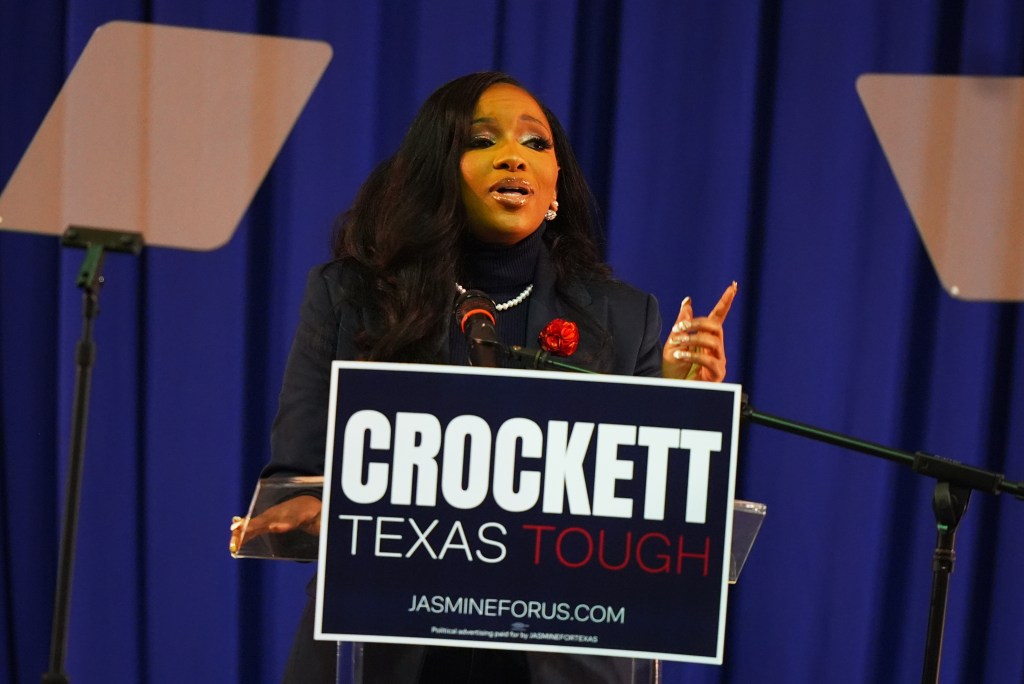 Rep. Jasmine Crockett speaking at a podium with a sign that reads "Crockett Texas Tough."