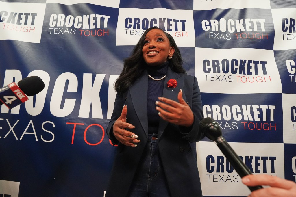 Jasmine Crockett speaks to reporters in front of a backdrop that reads "Crockett Texas Tough."