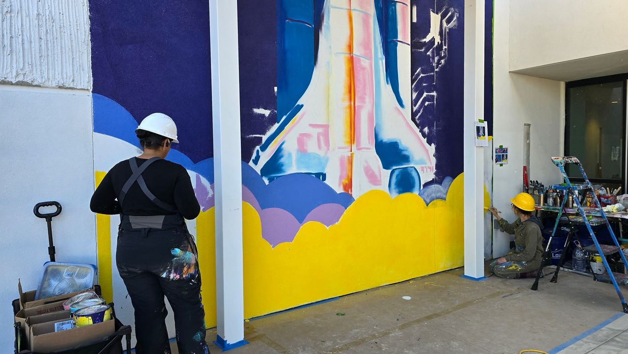 Muralists Michelle Wilson, left, and Allie Jenkins, right, work on an interactive mural at the Bledsoe-Miller STEAM Center ahead of the facility's grand reopening in January in Waco, Texas. The artwork will incorporate augmented reality elements designed to engage visitors. (Spectrum News 1/Agustin Garfias)