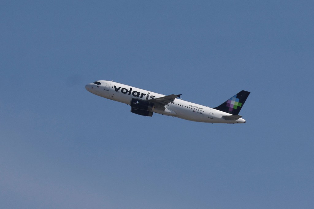 A Volaris airplane takes off from Felipe Angeles International Airport (AIFA) against a clear blue sky.