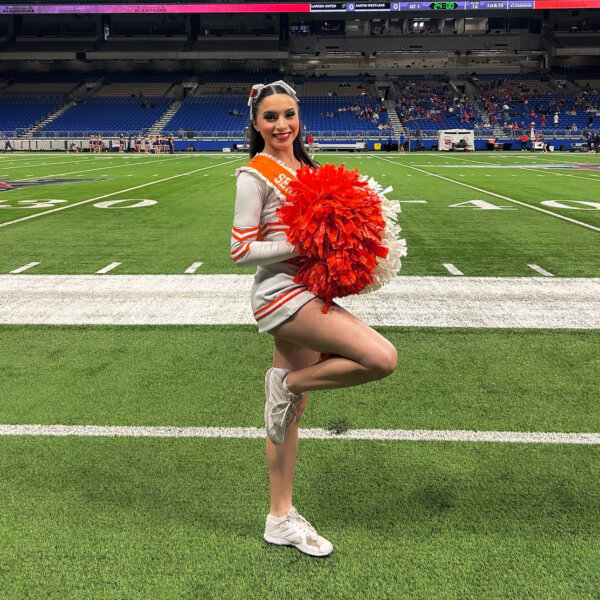 Brianna Aguilera with pom poms in a cheerleading uniform on a football field