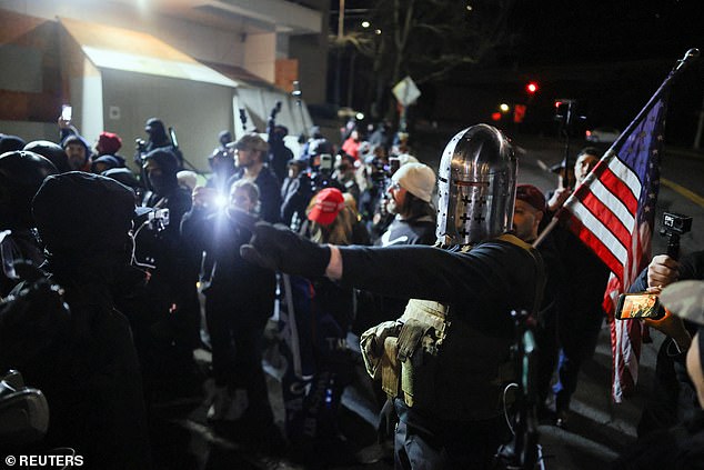 A counter-protester, who described themselves as a white christian nationalist and is wearing a medieval helmet, stands near people who gathered during a vigil in Portland