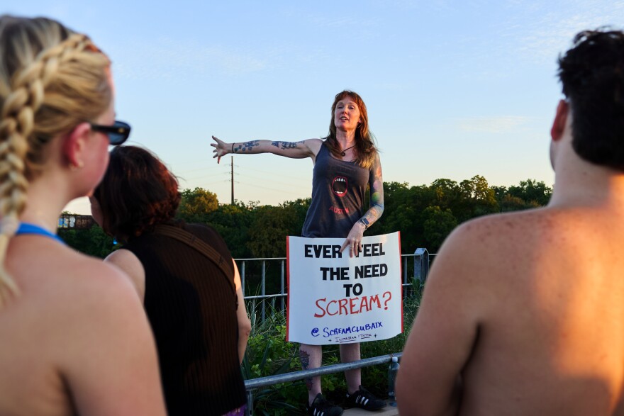 Krystal Morris stands by the railing on the bridge, holding a sign that says, "Ever feel the need to scream?" 