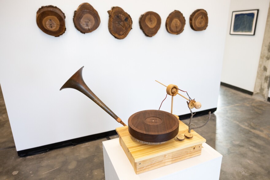 A record player made out of wood sits on a pedestal with round slices of a tree hanging on the walls in the background. 