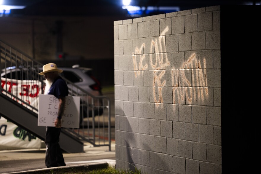 ICE out of Austin is spray painted on a building as a man carrying a protest sign walks by. 
