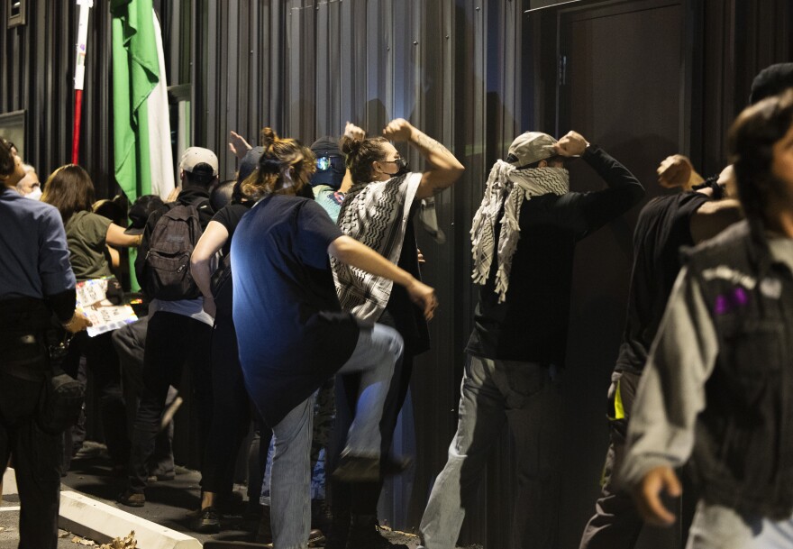Protesters bang on the outside of a building built of metal. 