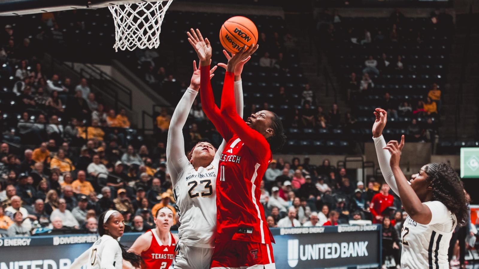 Texas Tech guard Bailey Maupin, wearing a red No. 20 jersey, looks up and drives a shot toward the basket as West Virginia defenders contest in front of a packed arena.