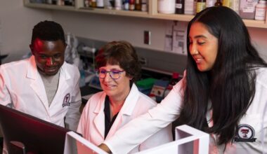 three biotechnology experts in lab coats look at a screen
