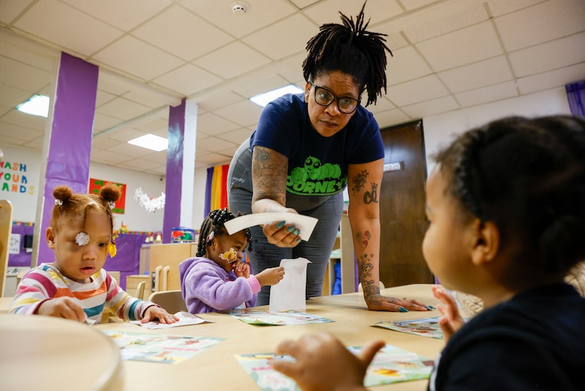 Carla Wright (center), toddler program teacher, helps 2-year-old Auri Johnson (right) with a...