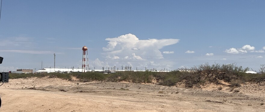 The tops of large white tents are visible in the distance in the desert at Fort Bliss.  The massive immigration detention camp houses people from across the country and is a hub for the Trump administration mass deportation effort.