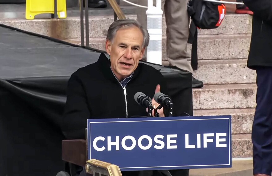 A man in a wheelchair speaks at a podium with a sign on it that reads "Choose Life."