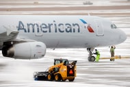 Ground crews ready an American Airlines jet for take off as others clear sleet from the...