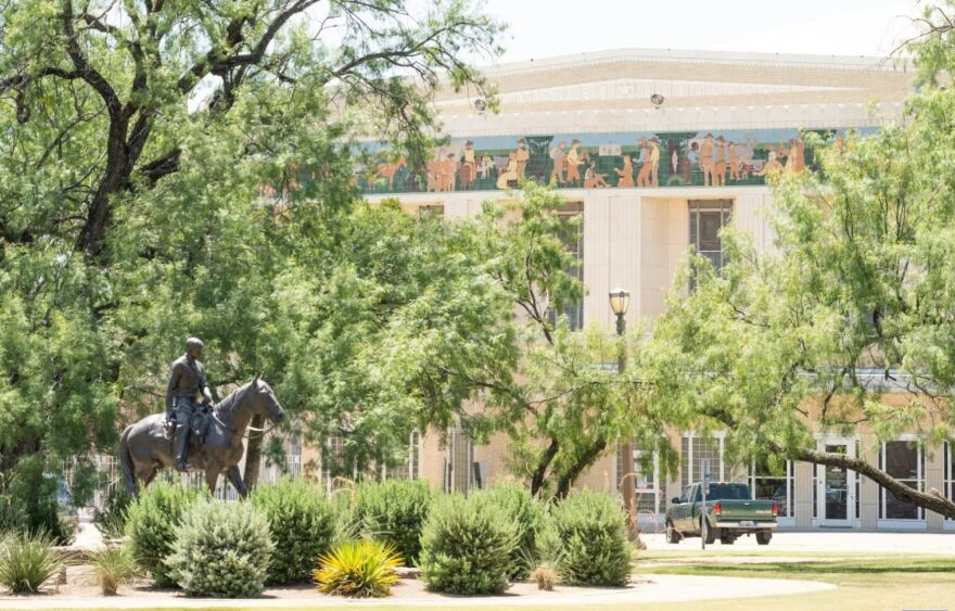 A photo of the exterior of the Will Rogers Memorial Center, with the statue of a horseman in front and tiled murals along the top of the building.