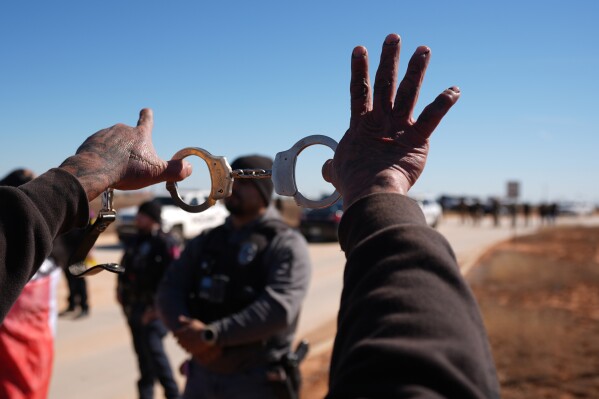A protester holds up handcuffs to taunt a police officer during a demonstration outside the South Texas Family Residential Center detention facility where Liam Ramos and his father are being detained in Dilley, Texas, Wednesday, Jan. 28, 2026. (AP Photo/Eric Gay)