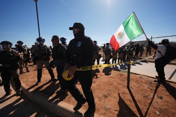 A police officer uses barricade tape to contain protesters gather outside the South Texas Family Residential Center detention facility where Liam Ramos and his father are being detained in Dilley, Texas, Wednesday, Jan. 28, 2026. (AP Photo/Eric Gay)