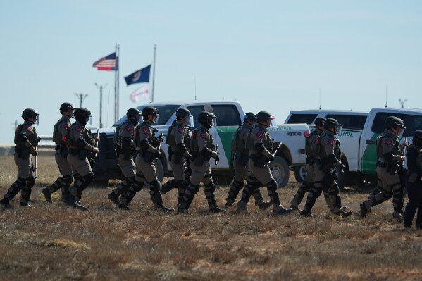 Texas state troopers wearing riot gear arrive to help disperse protesters gathered outside the South Texas Family Residential Center detention facility where Liam Ramos and his father are being detained in Dilley, Texas, Wednesday, Jan. 28, 2026. (AP Photo/Eric Gay)