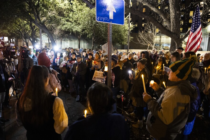 People gather in a group holding candles outside. 