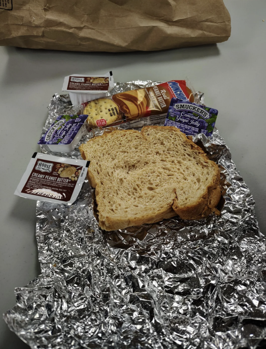 A photo of a slice of bread, crackers and packs of jelly and peanut butter on a crumpled sheet of aluminum foil