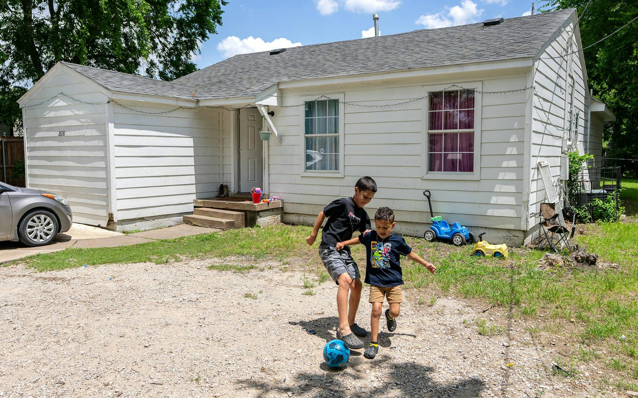 May 10 1:01 P.M. Carlos Rivera, 12, left, and his brother Christhofer Perdomo, 6, play soccer outside their family’s home in South Dallas.