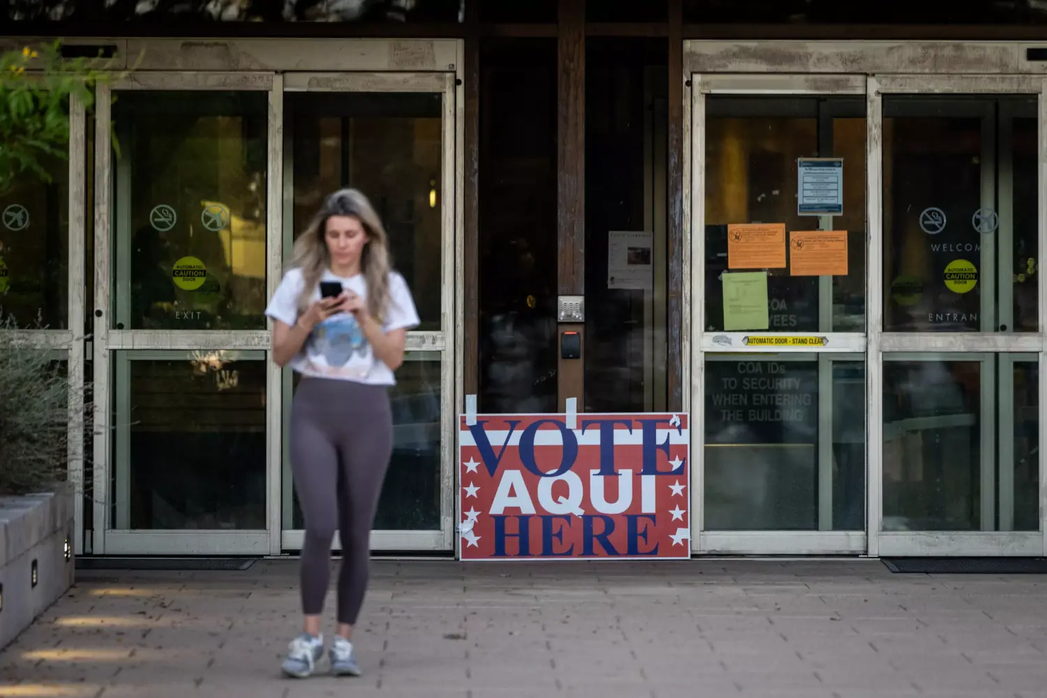 A person walks away from a building with a sign out front that says, "Vote Aqui Here."