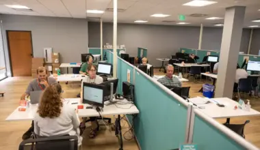 People gather around computers with privacy screens separating them in a nondescript office building.