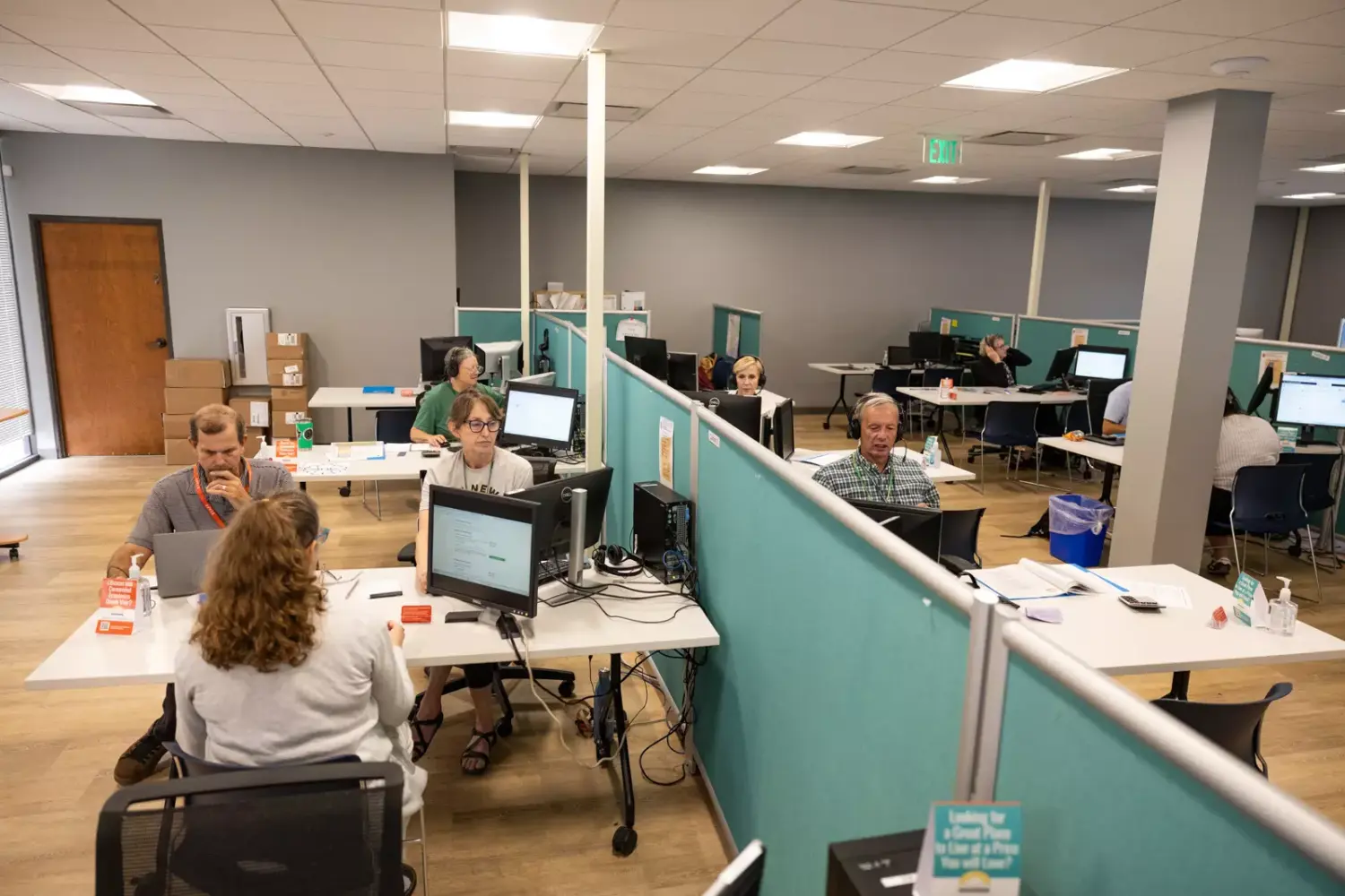 People gather around computers with privacy screens separating them in a nondescript office building.
