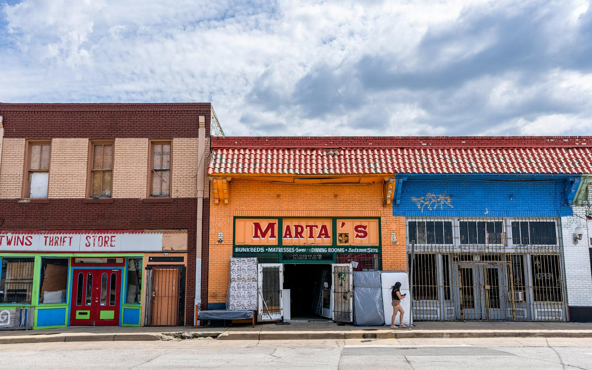 May 10 3:29 P.M. A woman walks past a row of thrift stores, including Marta’s, which sells bunk beds, mattresses, and furniture, on East 10th Street in Dallas.
