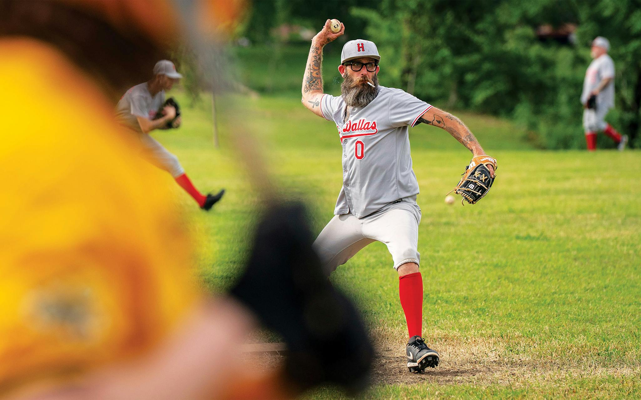 May 10 4:59 P.M. Josh Yingling, 48, smokes a cigarette as he warms up to pitch for the East Dallas Boozehounds, a team in the Oak Cliff Sandlot baseball league, during a game against the River City Honey Busters at Lake Cliff Park in Dallas. Yingling is also a restaurateur who opened Goodfriend Beer Garden and Burger House and Fortunate Son, a pizzeria in Garland.