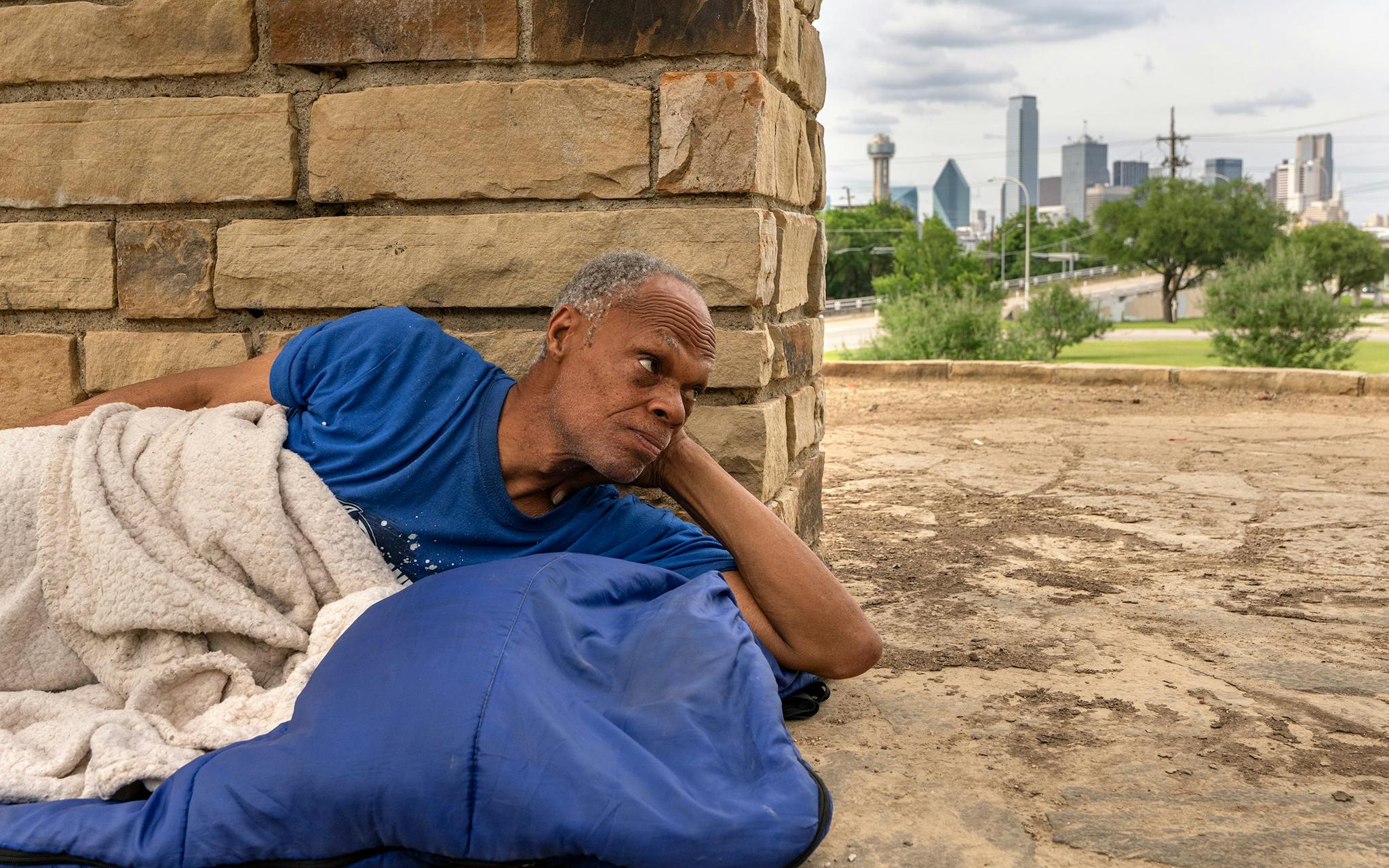 May 10 5:49 P.M. Anthony Hall, 63, lies on his sleeping bag under a pergola overlooking downtown at Oak Cliff Founders Park. Hall, who once played the bass drum in the Wilmer Hutchins High School marching band, said, “I’m not doing too much of nothin’ today. I’m just taking it easy, trying to get my feet healed up. They swell up when I walk a lot. I do a lot of walking, so I’m just staying off of ‘em a little bit.”